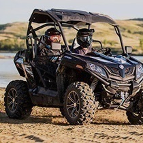 A couple sits in a UTV in a muddy river setting.