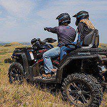 A man sits on an ATV and points into the distance while a woman sits behind him.